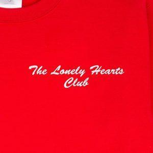 "The Lonely Hearts Club" embroidered in blanc thread on a red sweatshirt: front-on close-up