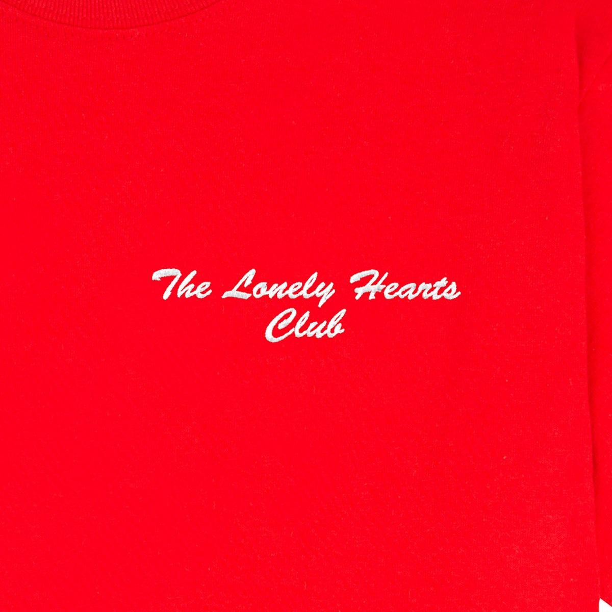"The Lonely Hearts Club" embroidered in blanc thread on a red tee: front-on close-up